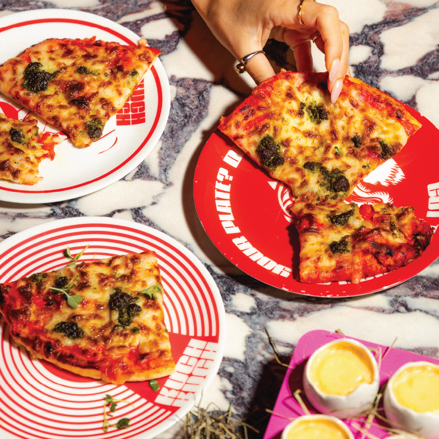 Kuch Kuch branded pizza slices and egg shell-style cocktail serves on a marble table at a creative cocktail bar in St Julian’s, Malta.
